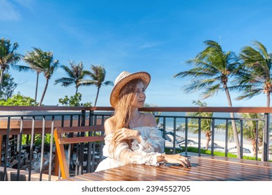 Palm trees shadowing wooden deck, woman in white and straw hat, overlooking tranquil ocean. Vacation destination. - Powered by Shutterstock