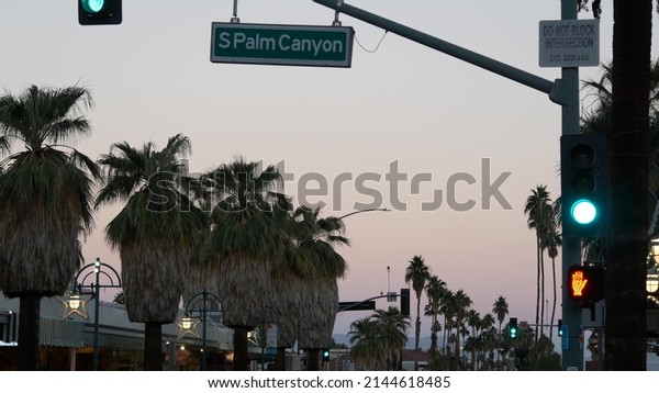 Palm trees and sky, Palm Springs street, city near
Los Angeles, semaphore traffic lights on crossroad. California
summer road trip on car, travel USA. Road sign Palm canyon,
twilight dusk after sunset