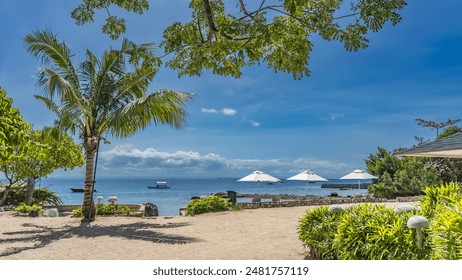 Palm trees and tropical plants grow on the oceanfront. Sun loungers, beach umbrellas in the distance. Boats in the turquoise sea. A green branch against a  blue sky and clouds. Philippines. Cebu. - Powered by Shutterstock