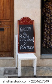 PALMA DE MAJORCA, SPAIN - MAY 23, 2018:   Sign For Paella Propped Up On A Chair Outside Restaurant