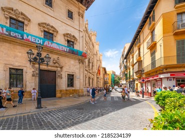 Palma de Mallorca, Spain - June 7 2022: Tourists pass by city hall in the colorful, historic town square of the Spanish Mediterranean city of Palma de Mallorca, Spain, on the island of Mallorca.