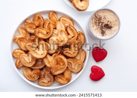  Palmiers, elephant ear, puff pastry cookie on a white plate and cup of cappuccino. Sweet homemade cakes. Traditional sweet puff pastry dessert with sugar. concept for valentine's day