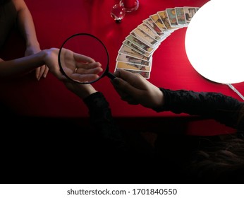 Palmistry Divine And Forecast Future Life From Asian Seer Woman Use Magnifying Glass Zoom On Hand Palm Within Spread Vintage Tarot Cards And Mystic Crystal Ball On Table In Dark Night