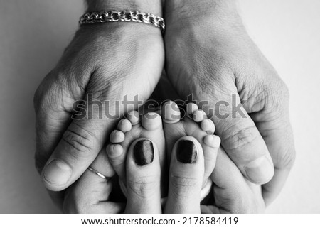 The palms of the parents. A father and mother hold a newborn baby by the legs. The feet of a newborn in the hands of parents. Photo of foot, heels and fingers. Black and white studio macro photography