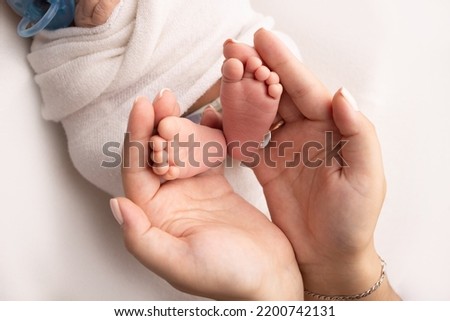 The palms of the parents. A father and mother hold the feet of a newborn child in a white blanket on a white background.. The feet of a newborn in the hands of parents. Photo of foot, heels and toes.