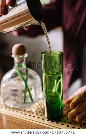 Paloma cocktail. Bartender pours cocktail from metal shaker into green highball glass.