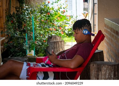 Palomino, Dibulla, La Guajira, Colombia - December 4 2021: Young Man Sitting on the Patio with a Headset and Looking at his Phone