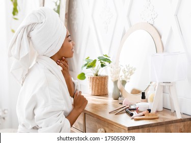 Pampering Day Concept. Attractive African Woman Wrapped in Bathrobe And Towel Sitting At Dressing Table, Ready For Beauty Treatments At Home