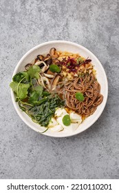 Pan Asian Style Vegetarian Soup On A Spicy Broth With Buckwheat Noodles, Mushrooms, Cilantro, Omelette And Tofu Cheese Over Gray Concrete Background. Overhead View, Copy Space