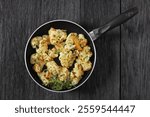 pan fried cauliflower florets on a skillet on dark oak wood table, horizontal view from above, flat lay