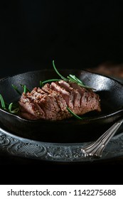 Pan fried wild boar fillet with seasoning and rosemary herb garnish in a iron skillet shot against a rustic background and wood burner stove. Copy space.