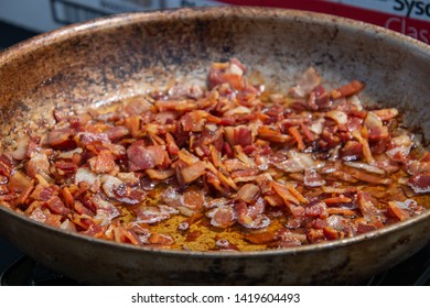 Pan full of pieces of bacon and onion with puddle of grease frying - Shutterstock ID 1419604493