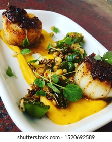 Pan Seared Scallops Topped With Bacon Jam With Shishito Peppers, Sweet Corn, Pork Sausage, And A Red Curry Squash Puree