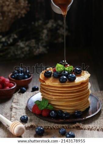 Foto Bild Pfannkuchen mit Johannisbeeren und Blaubeeren in gusseiserner Pfanne stehen auf dunklem Tisch