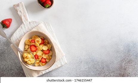 Pancake cereal, mini pancakes in a bowl with strawberries on gray background. Trendy food during quarantine and lockdown. Top view, copy space for text. Menu, recipe, banner. Kid's breakfast.