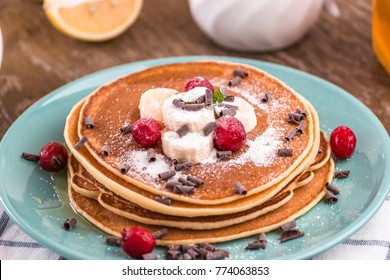 Pancake Stack  Covered With Honey, Chocolate Chips, Banana And Cranberries. On A Wooden Background In A Blue Plate