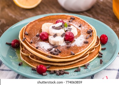 Pancake Stack  Covered With Honey, Chocolate Chips, Banana And Cranberries. On A Wooden Background In A Blue Plate