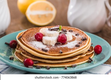 Pancake Stack  Covered With Honey, Chocolate Chips, Banana And Cranberries. On A Wooden Background In A Blue Plate