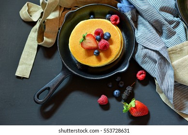 Pancakes with berries in the black pan. Decorated with tablecloth and fresh Strawberries, Raspberry, Blueberry.