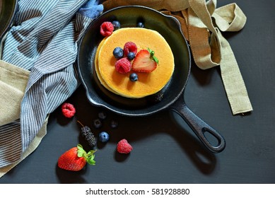 Pancakes with berries in the black pan. Decorated with tablecloth and fresh Strawberries, Raspberry, Blueberry.
