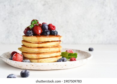 Pancakes with berries and maple syrup for breakfast on a light background.