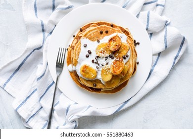 Pancakes with caramelized bananas, natural yogurt, chocolate chips and coconut shavings on white plate. Top view - Powered by Shutterstock