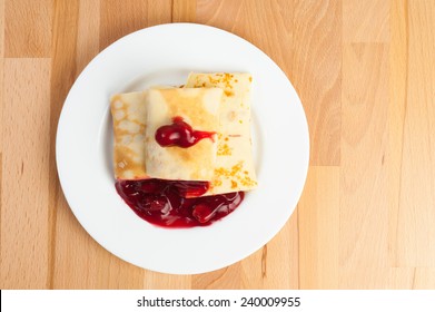 Pancakes With Cherry Jam On White Plate Placed On Wooden Surface, Top View