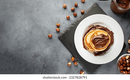 Pancakes with chocolate paste and hazelnuts, on a white plate on a background of concrete, slate with copy space for your text