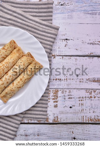 Pancakes with filling on a white plate. Wood background. Rustic style. Rolled up pancakes ready for eating. Wrapped thin pancakes. Stack of homemade thin crepes. Space for your text. 
