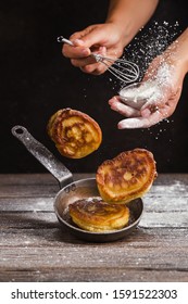 Pancakes And Frying Pan Levitate Over A Table, And A Man Holding A Whisk, Sprinkled With Flour