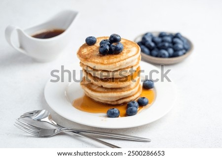 Pancakes stack with blueberries and maple syrup on white table background. Sweet morning pancake meal
