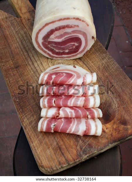 Pancetta, typical italian roll raw bacon with\
slices on wood\
trencher