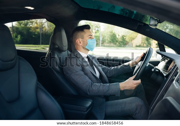 Pandemic. Citizens. Lockdown\
safety. Adult businessman wearing medical mask in prevention for\
coronavirus and driving his car to work. Businessman\
healthcare.