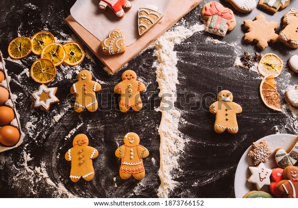 Pandemic cookies. Festive\
conceptual bakery. Social distancing. Decorated gingerbread man in\
protective mask divided from biscuits flour powder line on black\
desk.