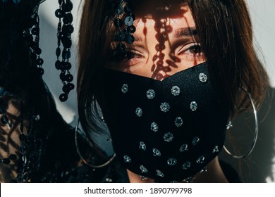 Pandemic Fashion. Night Club Party. Gypsy Style. Woman In Black Designer Decorated Crystal Beads Face Mask Looking At Camera Shadow Light.