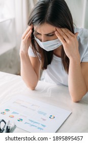 Pandemic Furlough. Office Quarantine. Lockdown Hardship. Disturbed Depressed Tired Woman In Protective Face Mask Suffering From Migraine Attack At Light Home Workplace.