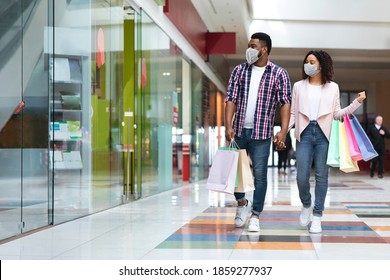 Pandemic Shopping. Black couple wearing protective face medical masks walking with shopper bags in mall, african american spouses making purchases during coronavirus quarantine, copy space