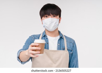 Pandemic, Social Distance. Takeaway Food. Young Asian Korean Man Barista Coffee Shop Assistant Holding Hot Beverage Decaf Coffee Tea In Mask Against Covid 19 Isolated On White Background