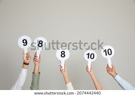 Panel of judges holding different score signs on beige background, closeup