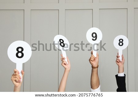 Panel of judges holding different score signs against light wall, closeup