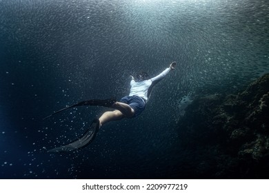 Panglao, Philippines - 28.04.2022: Male Freediver Fun Diving Swimming To The Surface Through A Cluster Of Sardines In The Ocean Sea Holding Breath