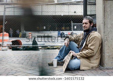 Panhandler sitting while blurred pedestrians pass him by