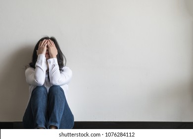 Panic attack woman, stressful depressed emotional person with anxiety disorder mental health illness, headache and migraine sitting feeling bad with back against wall on the floor in domestic home - Shutterstock ID 1076284112