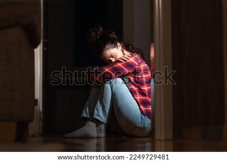 Panic disorder and obsessive-compulsive disorder. Crying young Caucasian woman sits down on floor in dark living room. Concept of psychology and mental problems.