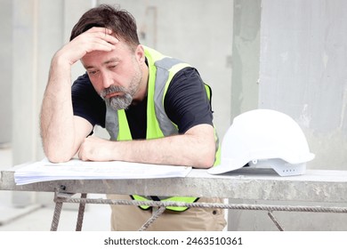Panic senior worker engineer foreman with safety vest and helmet put hand on head while staring at blueprint at construction site. Stressed worried elderly architect works at building site workplace.