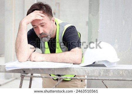 Panic senior worker engineer foreman with safety vest and helmet put hand on head while staring at blueprint at construction site. Stressed worried elderly architect works at building site workplace.