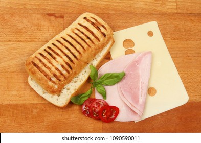 Panini ingredients, ham, cheese, tomato and basil on a wooden chopping board, top view
