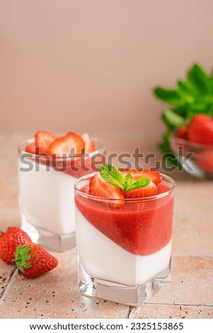 Panna cotta homemade Italian dessert of sweetened cream thickened with gelatin with layer or fresh strawberry sauce decorated with juicy berries and mint leaf served in glass on table with ingredients