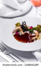 Panna Cotta With Smoked Eel And Balsamic Sauce, Top With Chuka Salad, Almond Flakes, Edible Petals, Gilded Nori Seaweed. The Food Is In A Deep White Plate. The Plate Is On A White Tablecloth, Cutlery 