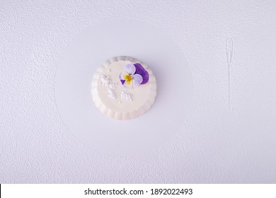 Panna Cotta Of White Cocolate And Wipped Cream Decorated With Edible Violet Flower Over On White Background With Dessert Spoon Trace.Top View. Overhead. Copy Space.